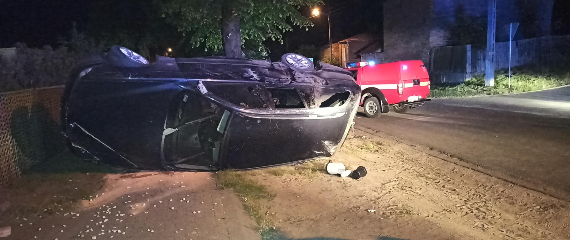 Na zdjęciu samochód osobowy leżący na boku na poboczu jezdni