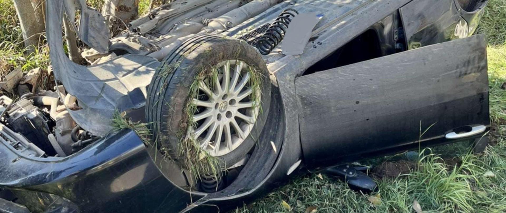 Samochód osobowy leży na dachu na poboczu drogi