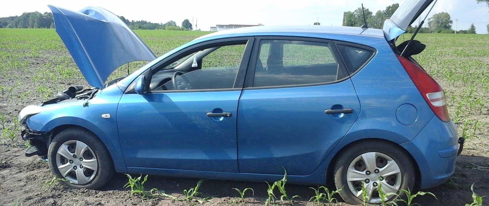 Samochód osobowy stojący na przydrożnym polu uprawnym. W aucie uszkodzony jest przód.