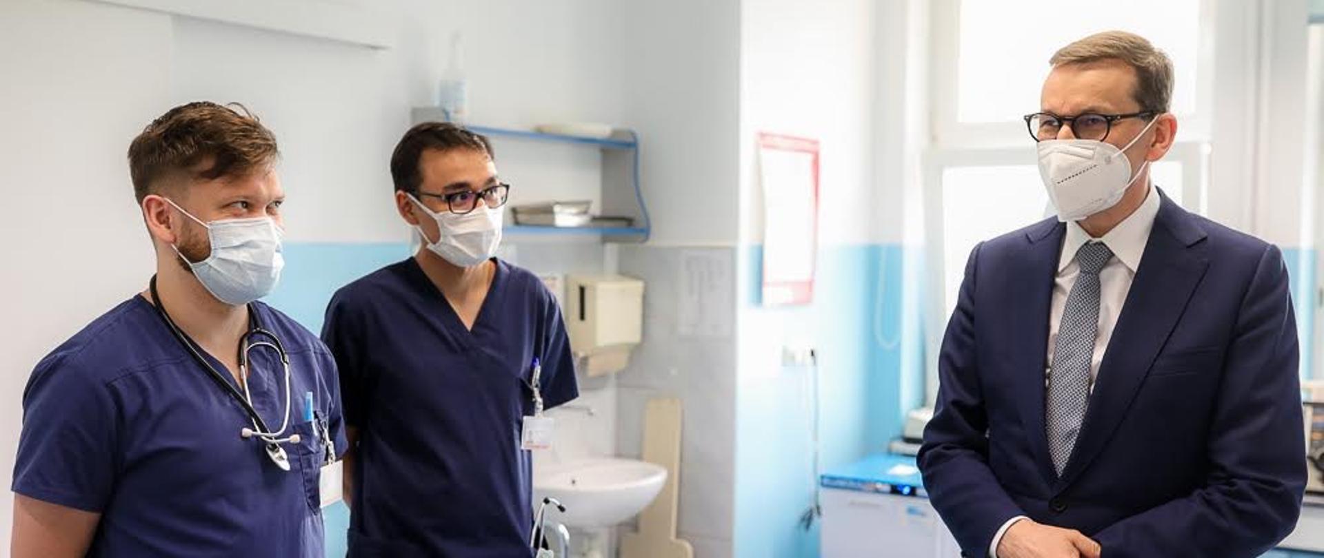 Premier stoi i rozmawia z lekarzami.