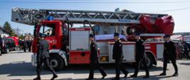 Czerwony pojazd straży pożarnej SD (samochód z drabiną) marki Magirus wykorzystywany jest w ceremonii pogrzebowej jako symboliczny karawan dla trumny strażaka. Strażacy PSP w czarnych mundurach wyjściowych z rogatywkami i złotymi obszyciami eskortują trumnę.