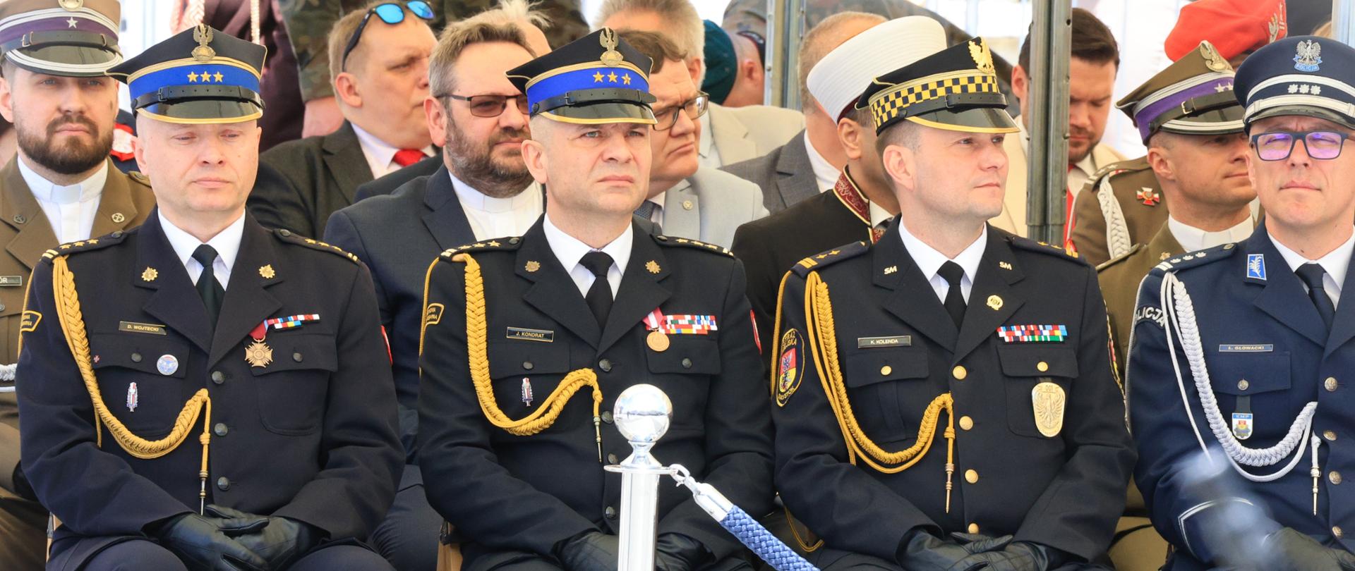Obchody Święta Narodowego 3 Maja - przedstawiciele służb mundurowych siedzą podczas uroczystości na krzesłach przodem do publiki, krzesła wygrodzone niebieskim sznurem, widać podlaskiego komendanta wojewódzkiego PSP i miejskiego PSP w Białymstoku