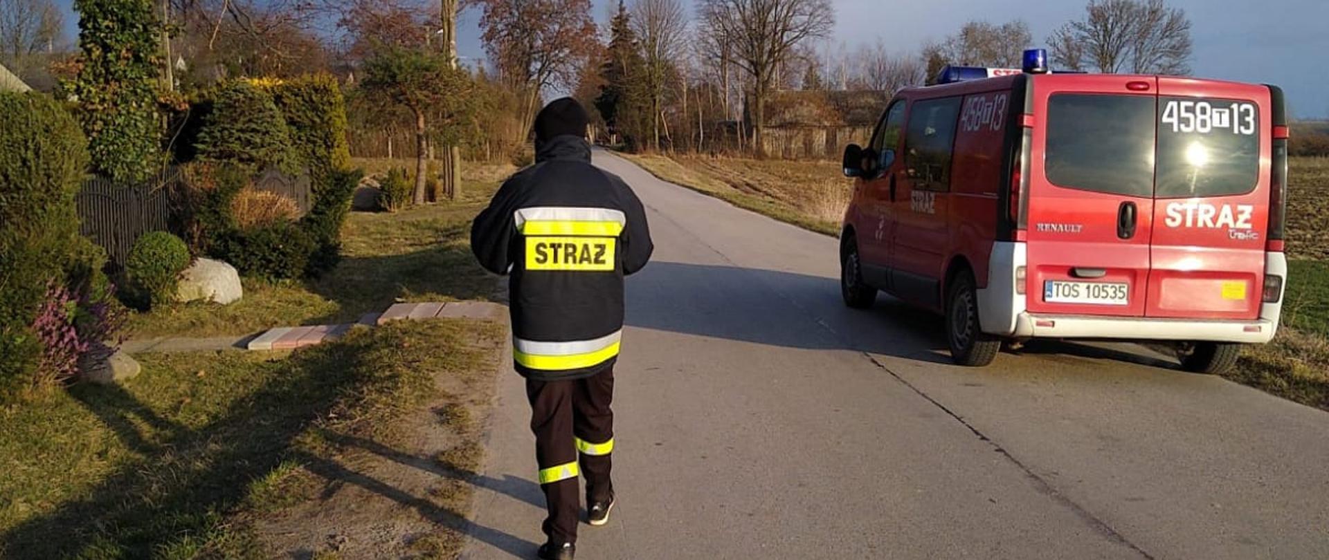 Strażacy roznoszą ulotki do gospodarstw domowych na terenie powiatu ostrowieckiego. Na zdjęciu widać strażaka przed domem mieszkalnym, który zostawia broszurę informacyjną.