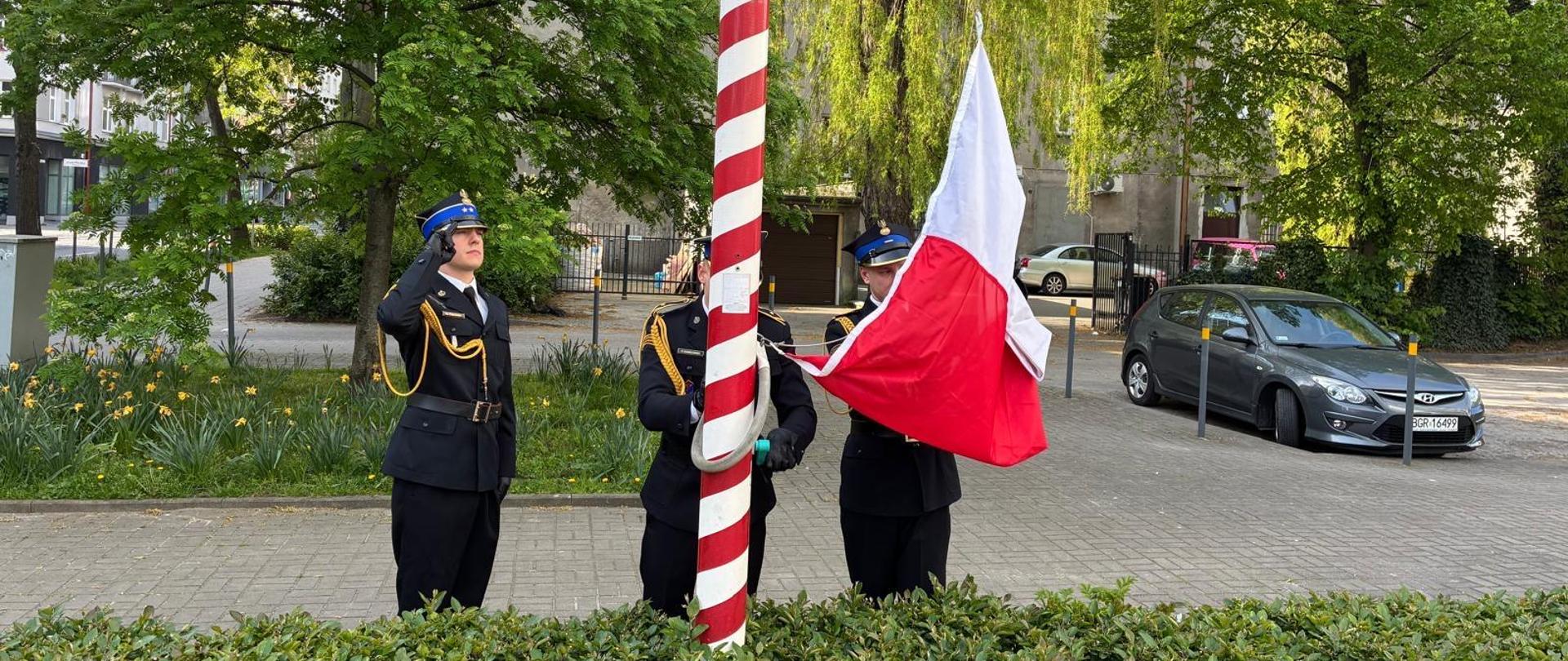 Funkcjonariusze PSP jako poczet flagowy stoją przy maszcie podczas mocowania flagi