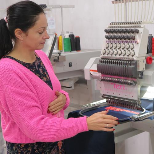 Kobieta stoi przy maszynie do szycia i patrzy na obrabiany materiał