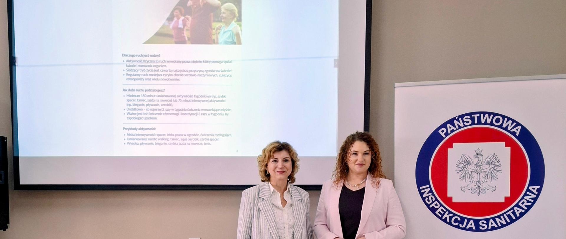 Przedstawicielki Państwowego Powiatowego Inspektora Sanitarnego w Garwolinie w czasie prezentacji poświęconej seniorom - w tle slajd, obok baner z logo Państwowej Inspekcji Sanitarnej.