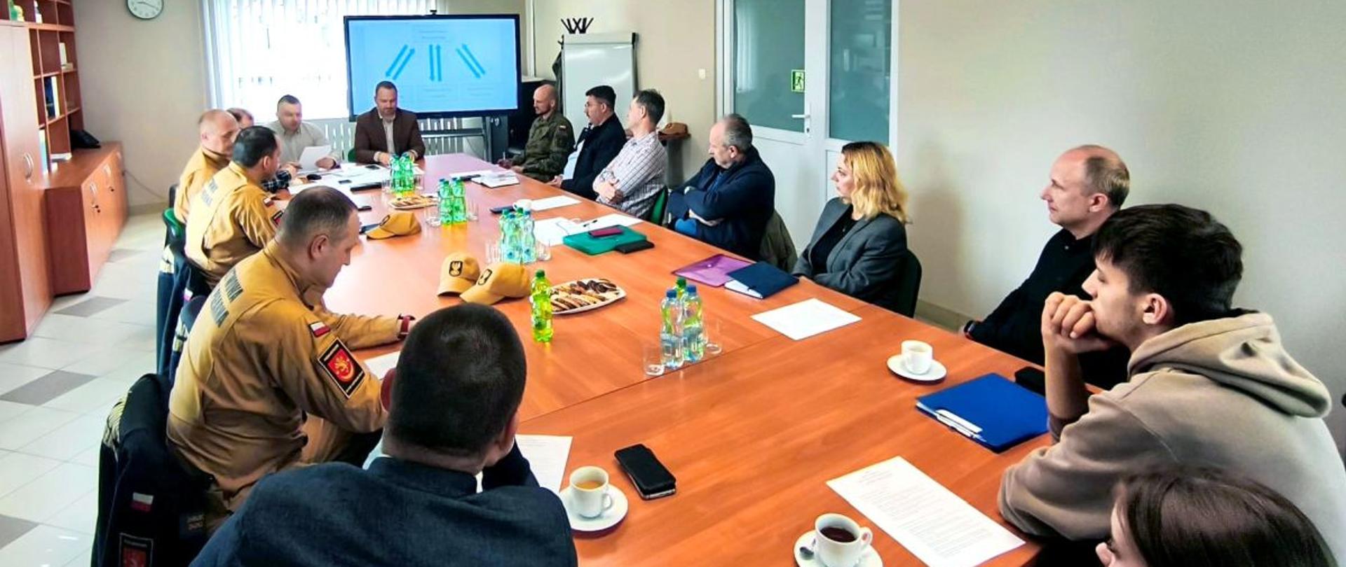 Zdjęcie przedstawia przedstawicieli służb mundurowych oraz samorządów lokalnych. Wszyscy siedzą przy dużym stole.