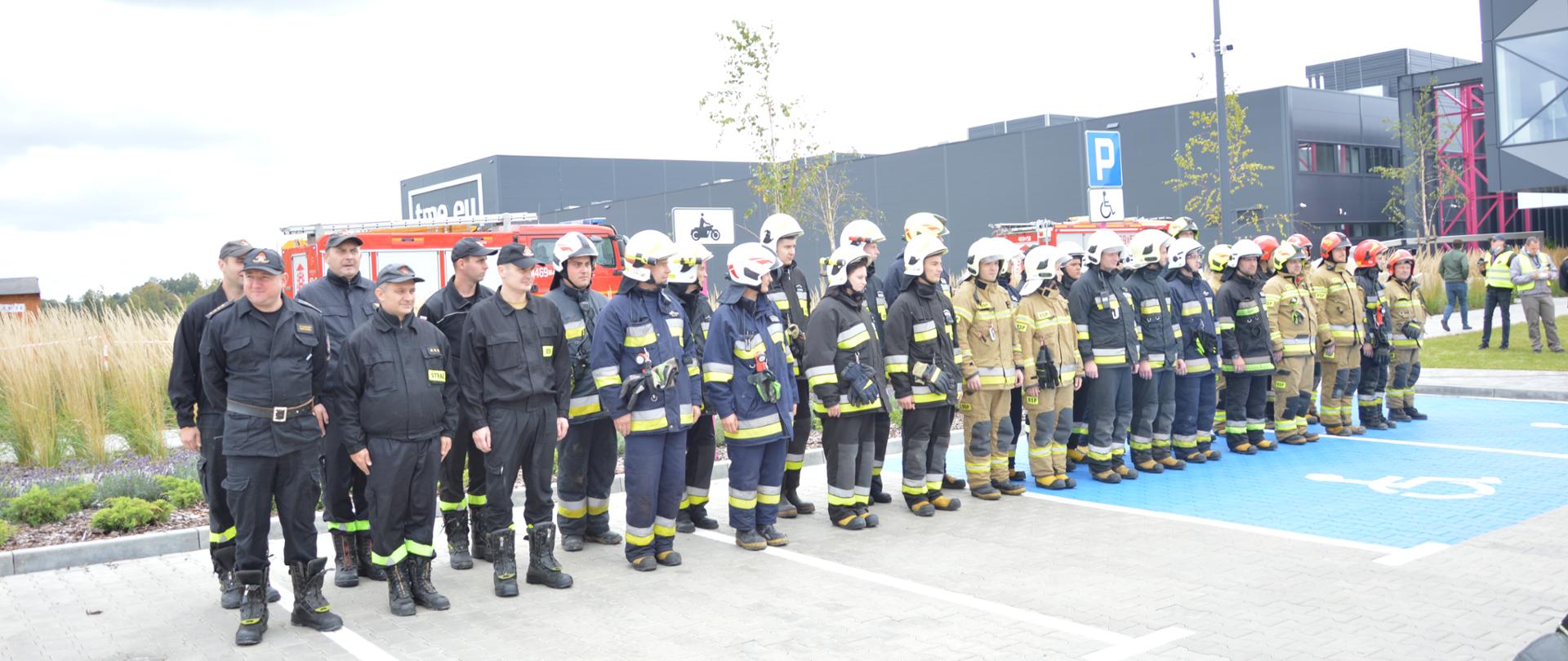 Zdjęcie przedstawia ćwiczących ratowników podczas zbiórki na zakończenie ćwiczeń. Widoczni są zarówno ratownicy PSP jak i OSP. 