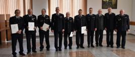 Zdjęcie obrazuje strażaków ochotników, którzy otrzymali decyzje o przyznaniu świadczenia ratowniczego. Pośród nich stoi Komendant Powiatowy wraz z zastępcą oraz funkcjonariusz odpowiedzialny za realizację wniosków.