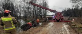 Dźwig strażacki podnosi przewrócony ciągnik rolniczy z rzeki. 