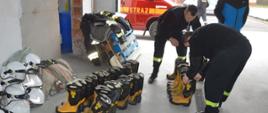 Sprzęt pożarniczy dla ukraińskich strażaków. Komenda Powiatowa PSP w Rawiczu. Strażacy przygotowują do transportu obuwie specjalne. Trwa ich przegląd. Oprócz obuwia w garażu znajdują się węże, hełmy, ubrania i europalety. W tle wóz strażacki.