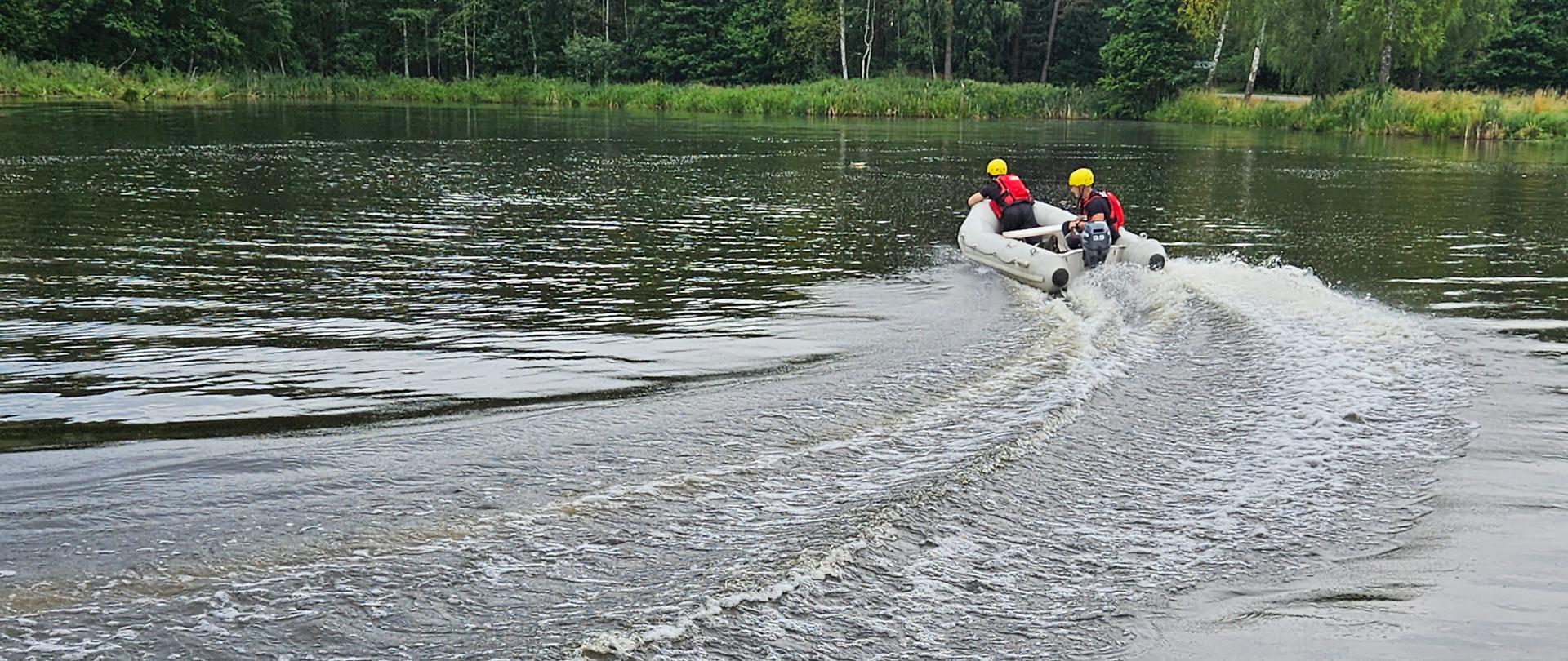 Strażacy pływający pontonem z silnikiem zaburtowym po akwenie wodnym „Biadaszek” w gminie Włoszczowa. Widoczny tył pojazdu. Sternik dokonuje manewru skrętu.