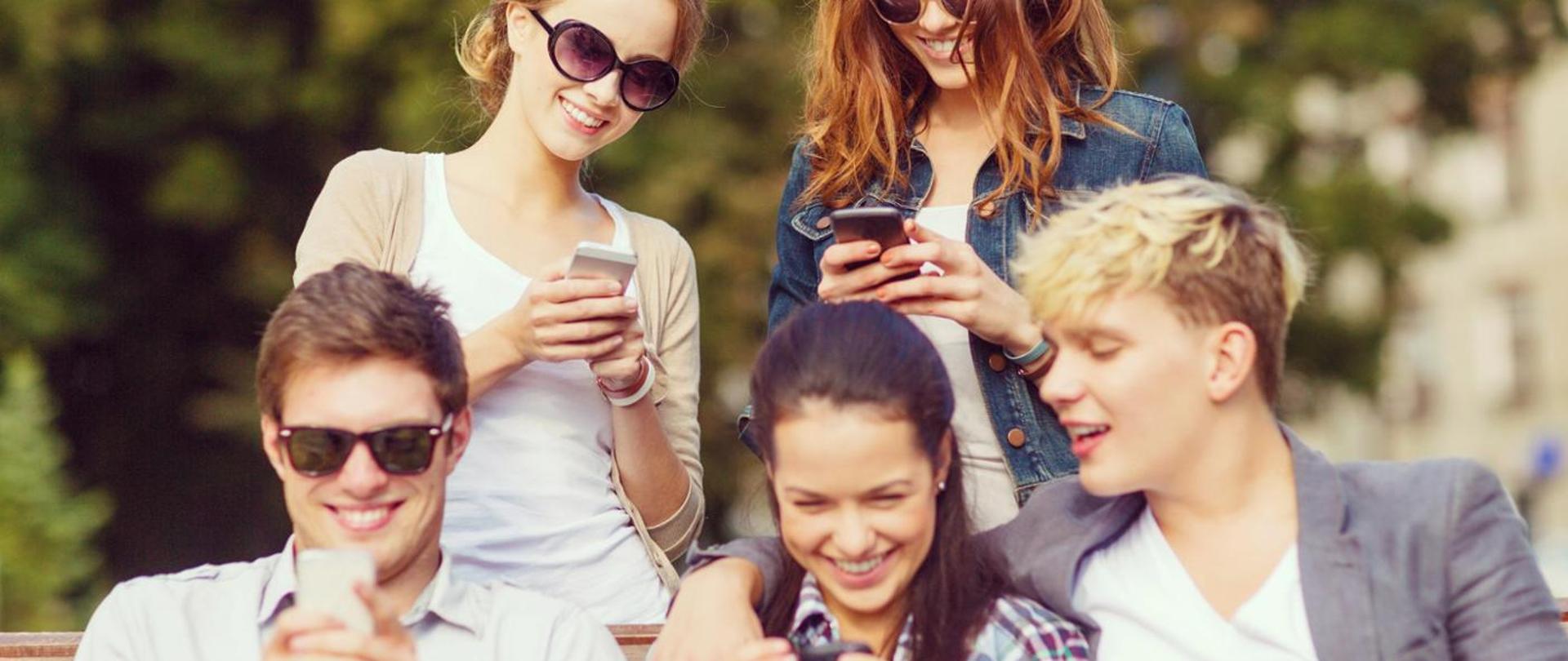 Pięcioro uśmiechniętych osób spoglądających w smartfony