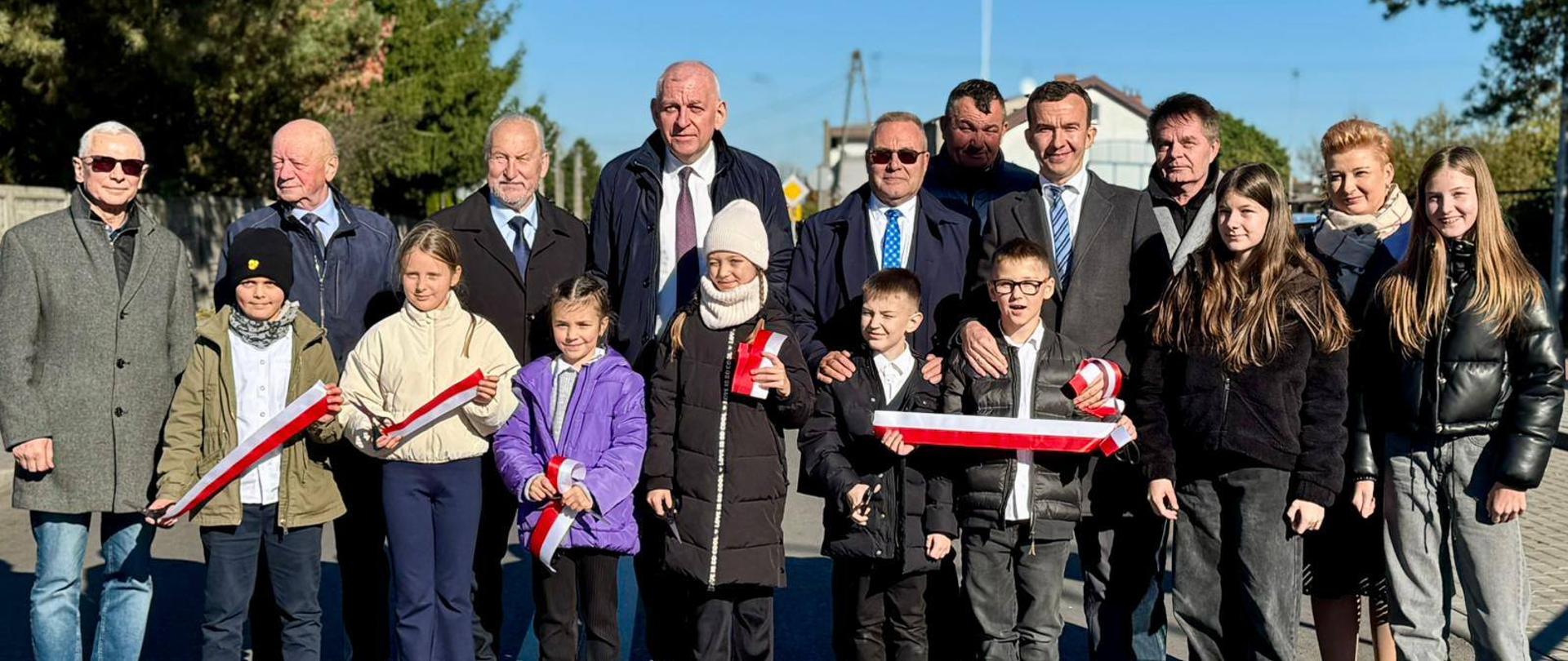 Kilkanaście osób przecina wstęgę na ulicy 