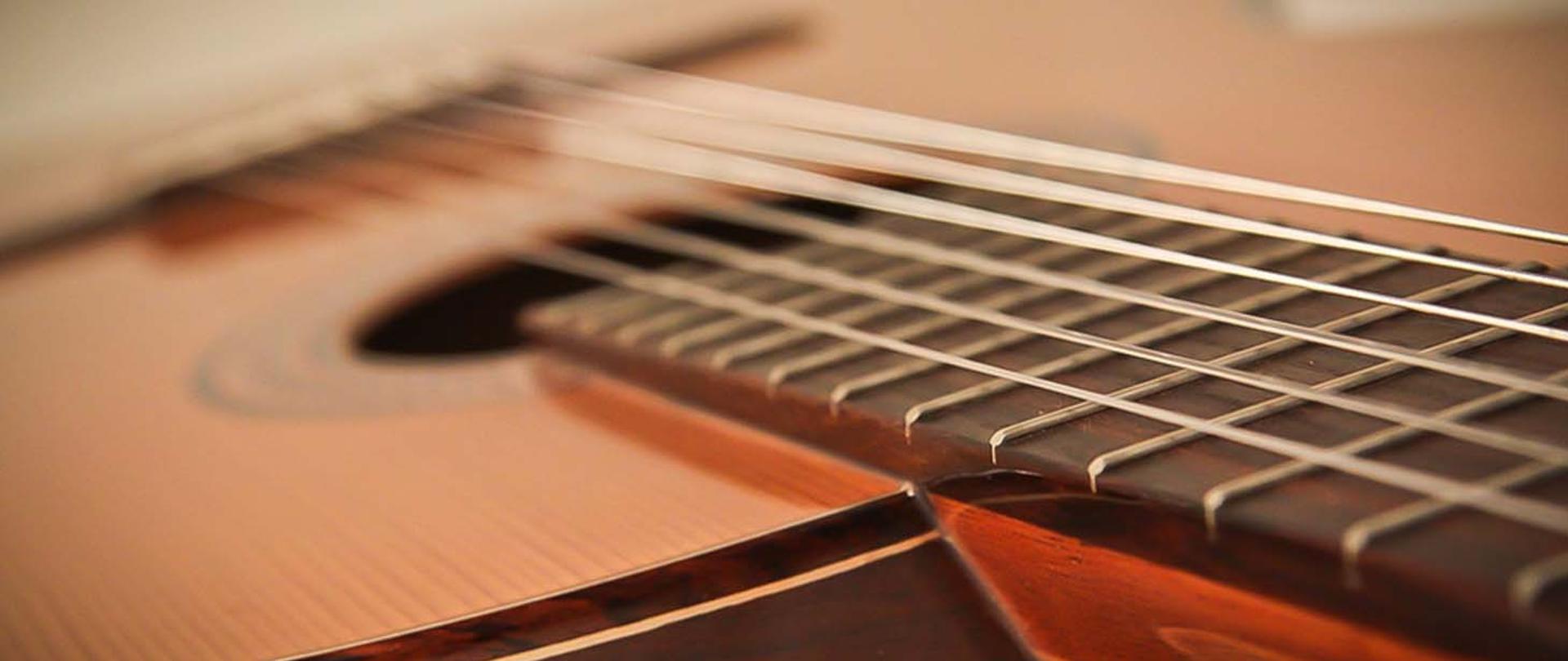 Zdjęcie przedstawiające fragment pudła rezonansowego i gryfu ze strunami gitary klasycznej.