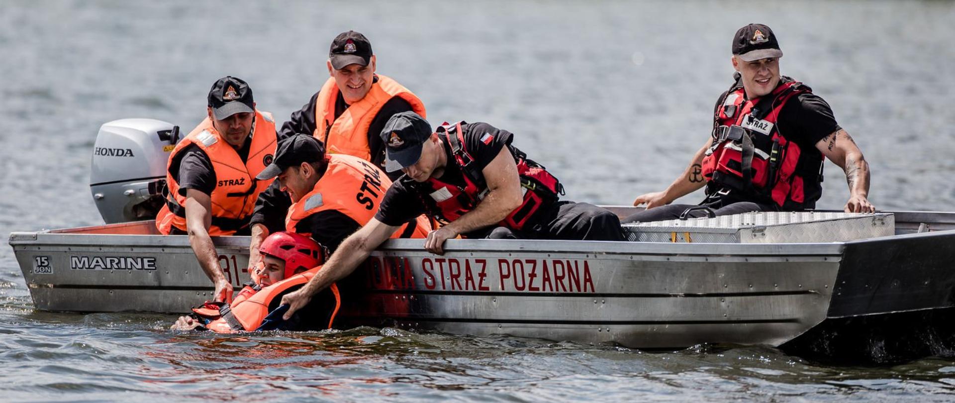 Strażacy w łódce wyciągają poszkodowanego z wody.