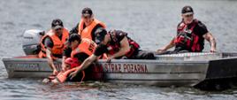 Strażacy w łódce wyciągają poszkodowanego z wody.