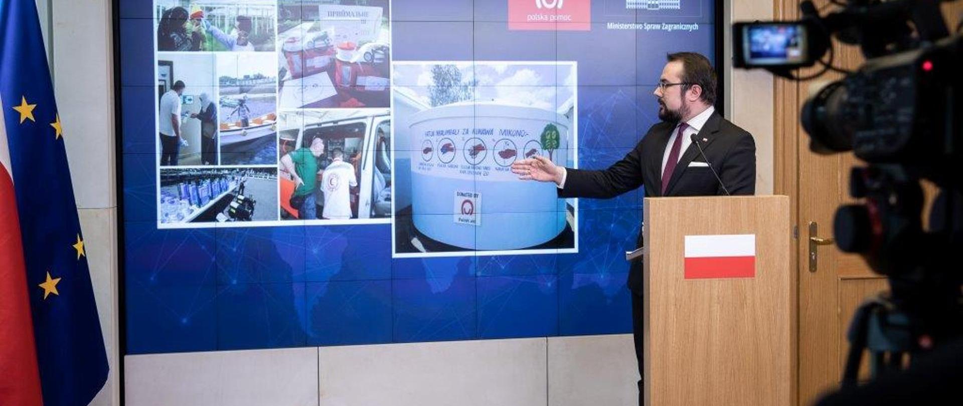 Wiceminister Paweł Jabłoński prezentuje zdjęcia z działania Polskiej pomocy