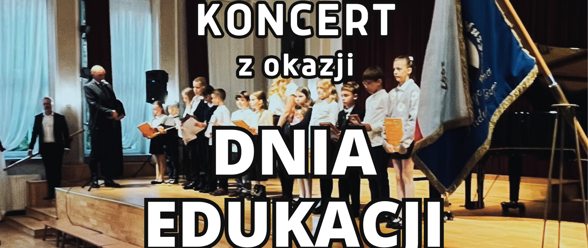 Na tle sceny ze stojącymi w rzędzie uczniami w uroczystych strojach biało-czarnych i napis Koncert z okazji Dnia Edukacji Narodowej