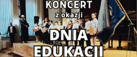 Na tle sceny auli gdzie w rzędzie stoją uczniowie ubrani w galowe stroje biało-czarne Napis Koncert z okazji Dnia Edukacji