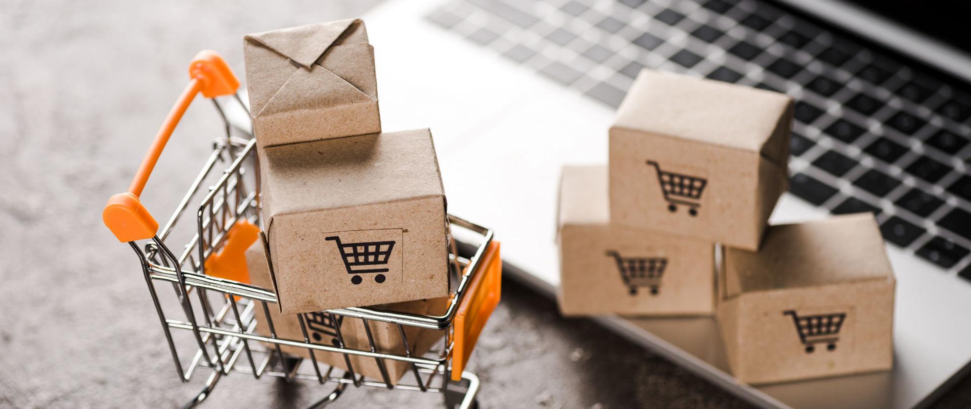 Klawiatura komputera, zabawkowy kosz na zakupy i kartony.