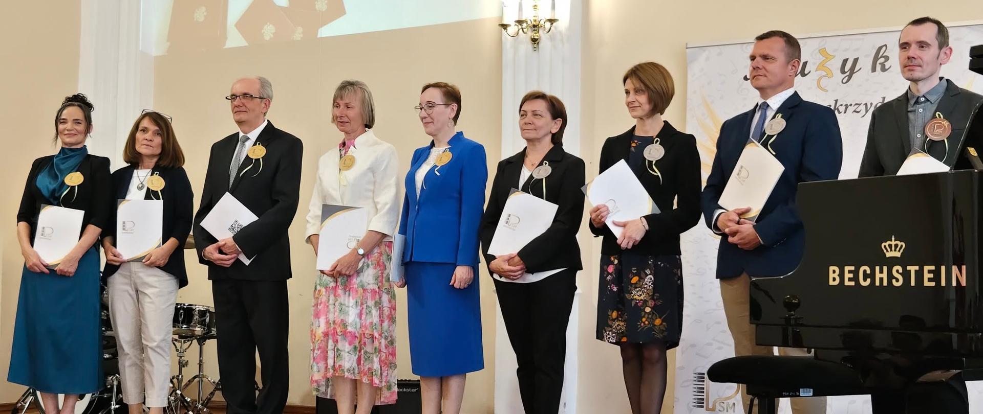 Dyrektor Sonia Wachowska wraz z pracownikami szkoły na scenie w sali koncertowej podczas wręczenia odznaczeń za Długoletnią Służbę 28.05.2026