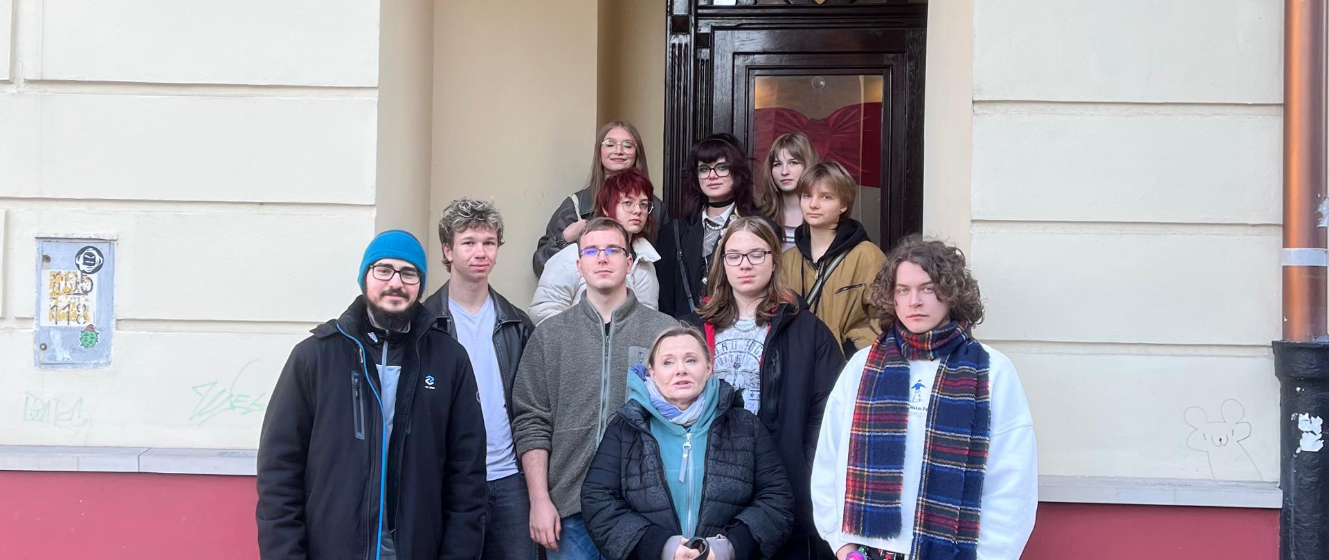 Na zdjęciu grupka młodzieży stoi przed wejściem do kamienicy, w której zlokalizowana jest siedziba wystawy "Niewidzialny dom". Za chwilę wejdą do środka by poznać jak to jest "widzieć" świat będąc niewidoma osobą.