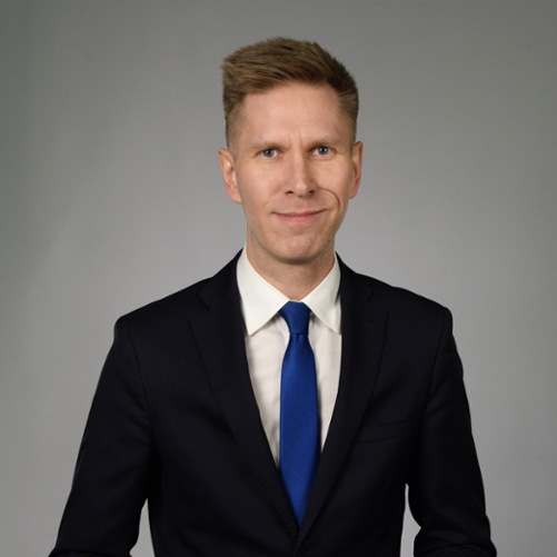Man in a black suit with a blue tie on a grey background.
