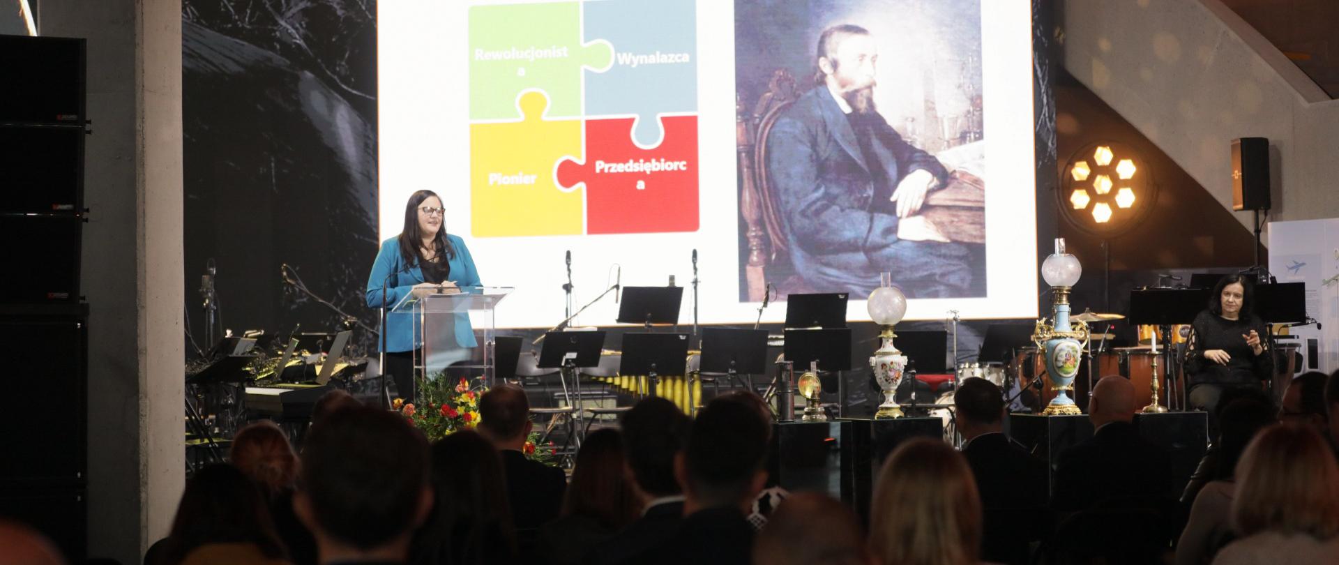 Wiceminister Małgorzata Jarosińska-Jedynak na scenie w mównicy. Przed nią publiczność.