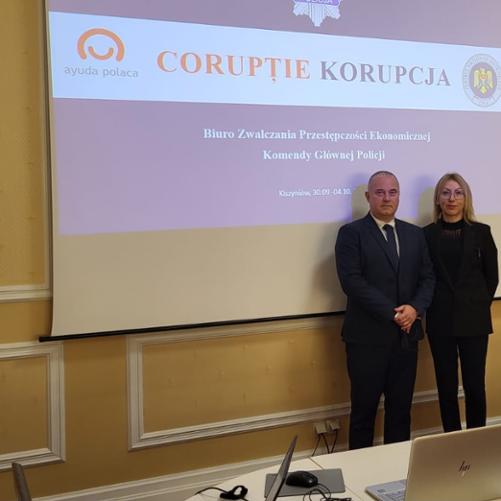Kobieta i mężczyzna na tle ekranu z napisem Biuro Zwalczania Przestępczości Ekonomicznej Komendy Głównej Policji i logo Polska Pomoc