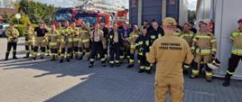 Zdjęcie przedstawia strażaków na zbiórce na terenie zakładu za strażakami samochody pożarnicze 