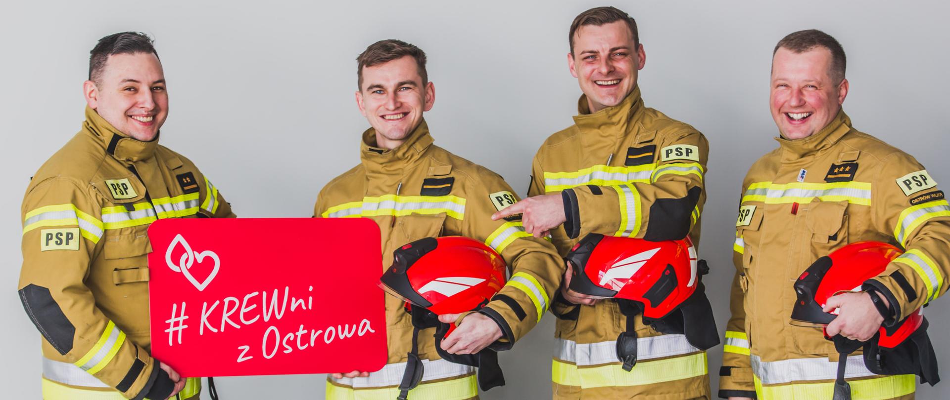 Czterech strażaków w ubraniach specjalnych stoi na jasnym tle, trzymając w rękach karty z hasłami promocyjnymi.