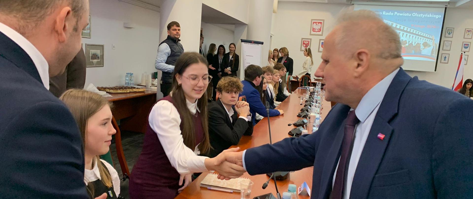 Mężczyzna w garniturze, wicewojewoda, podaje rękę elegancko ubranej nastolatce