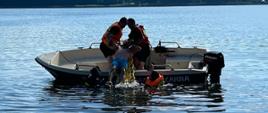 na zdjęciu czterech strażaków podejmujących osobę tonącą na łódź, w tle Jezioro Miejskie