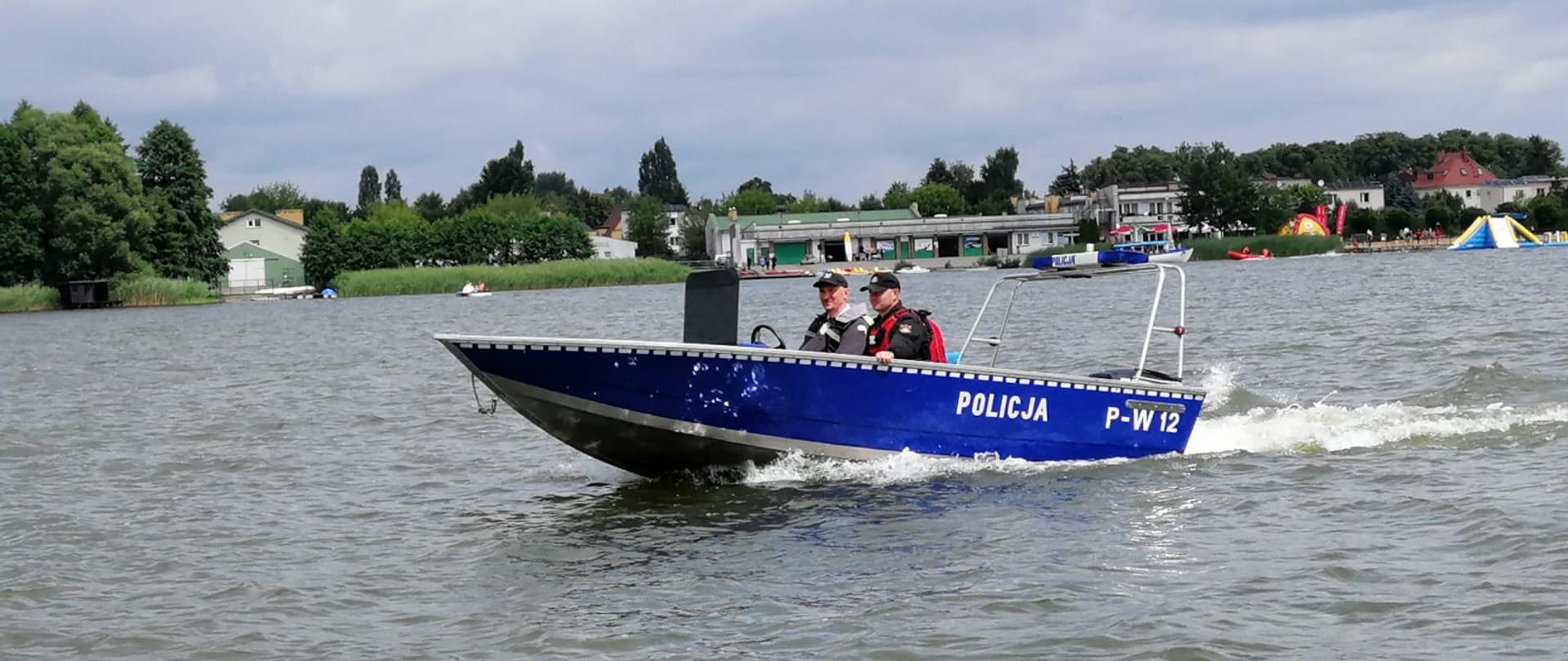 Zdjęcie przedstawia policjanta i strażaka w łodzi policyjnej podczas patrolu na jeziorze Raduń