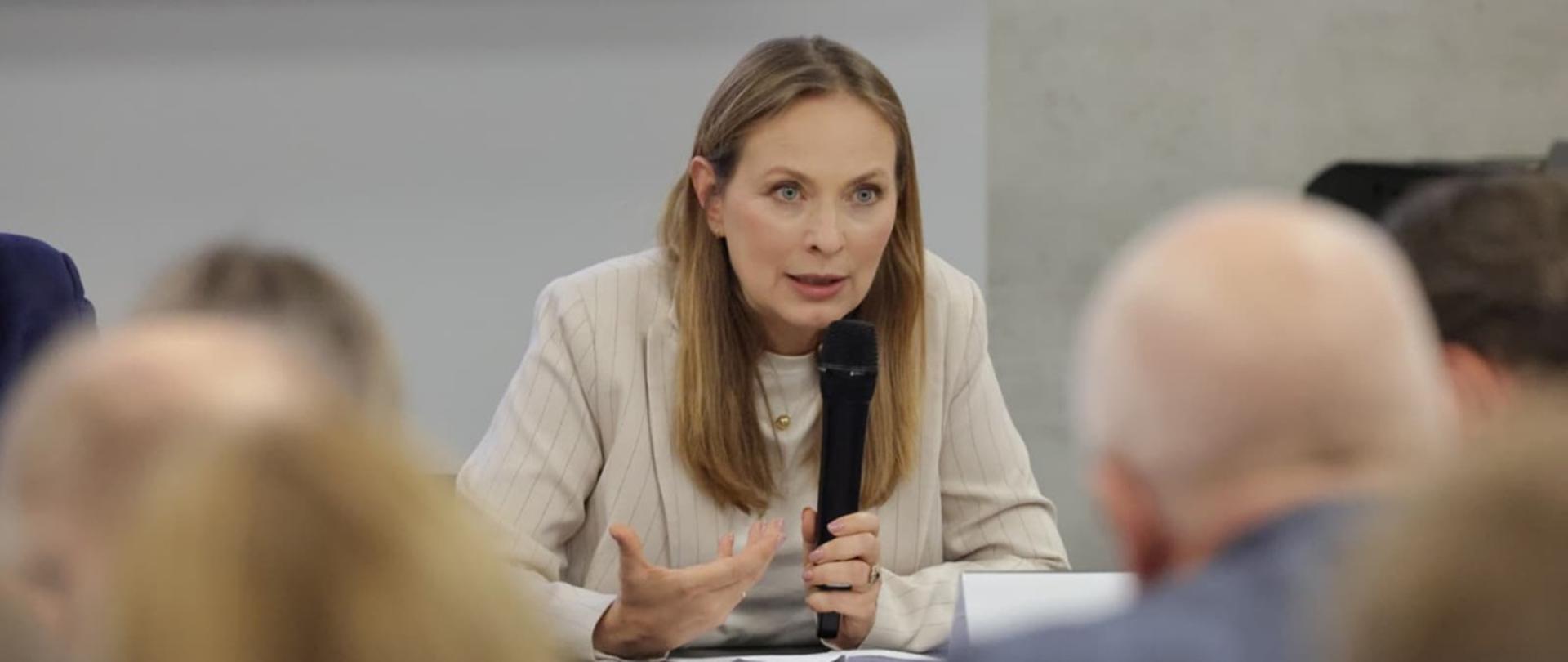 Minister funduszy i polityki regionalnej Katarzyna Pełczyńska-Nałęcz na spotkaniu z przedsiębiorcami woj. opolskiego, minister siedzi przy stole i przemawia do mikrofonu