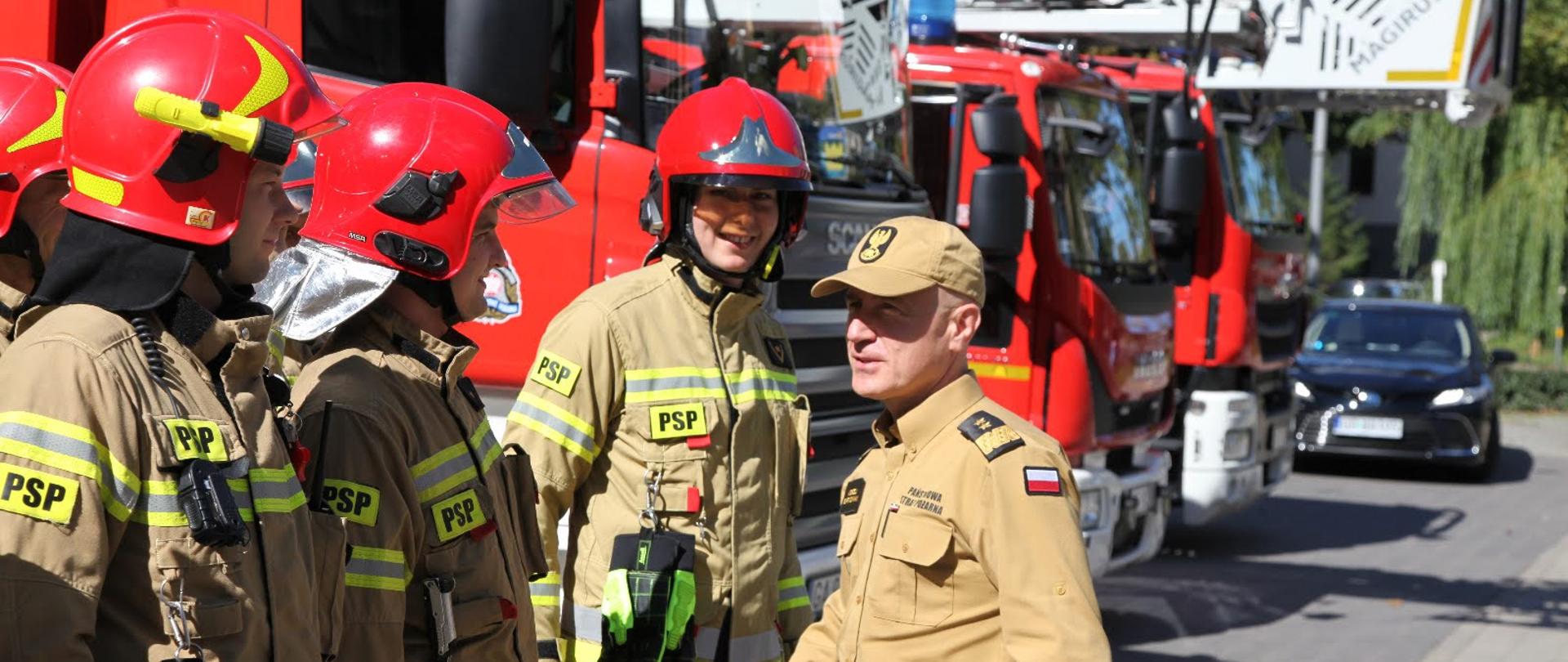 Komendant główny Państwowej Straży Pożarnej wita się ze strażakami ubranymi w hełmy oraz ubranie specjalne.