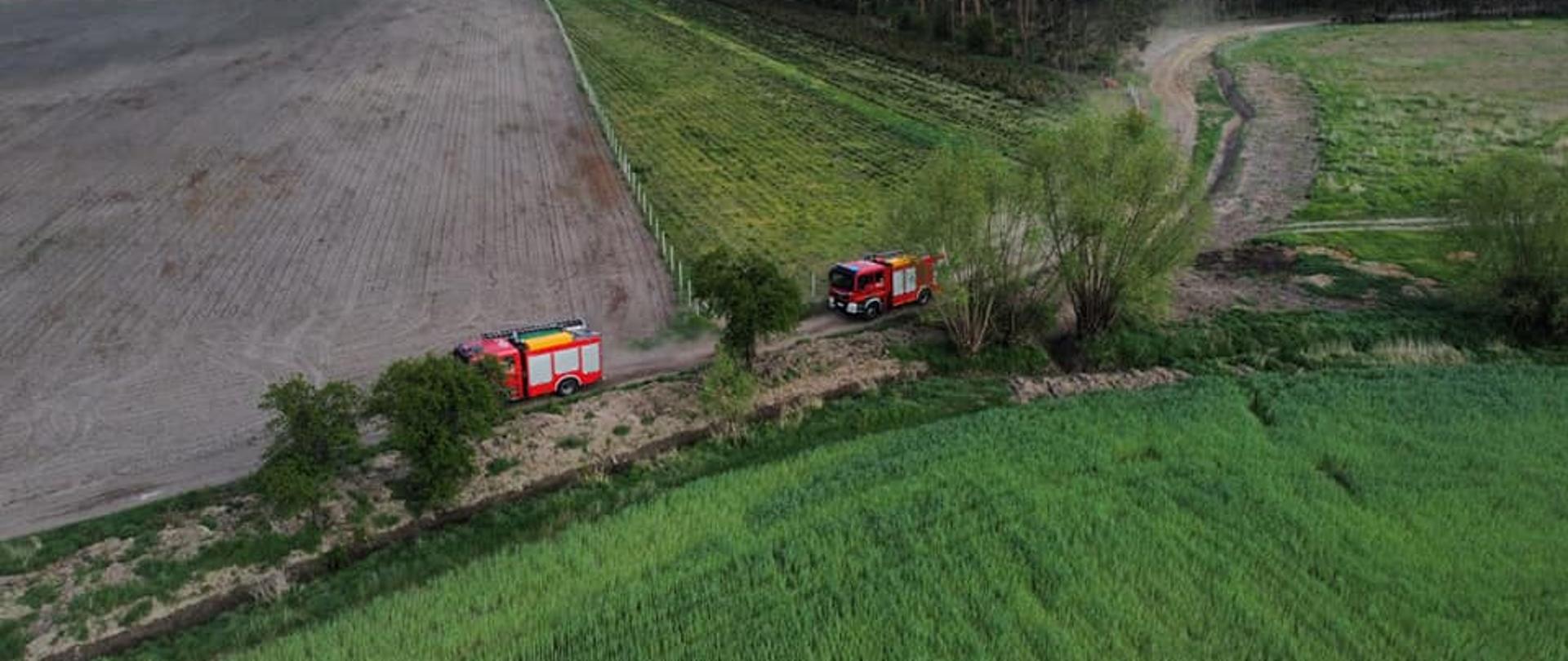 Zdjęcie z lotu ptaka, przedstawia pojazdy pożarnicze stojące na polnej drodze.
