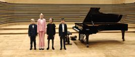 Dwie dziewczynki i dwóch chłopców stoi na estradzie przy fortepianie.