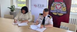 Dyrektor Zakładu Emerytalno-Rentowego Ministerstwa Spraw Wewnętrznych i Administracji. Pani Małgorzata Zdrodowska oraz Komendant Główny Państwowej Straży Pożarnej nadbrygadier Andrzej Bartkowiak siedzą przy stole prezydialnym i podpisują porozumienie. W tle rozwieszony baner z logo KG PSP i ZER MSWiA.