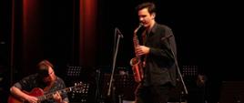 Zdjęcie przedstawia absolwentów PSM I stopnia w Jarocinie występujących na scenie. Krzysztof Szymenderski na gitarze towarzyszy Kacprowi Słaboszewskiemu grającemu na saksofonie.