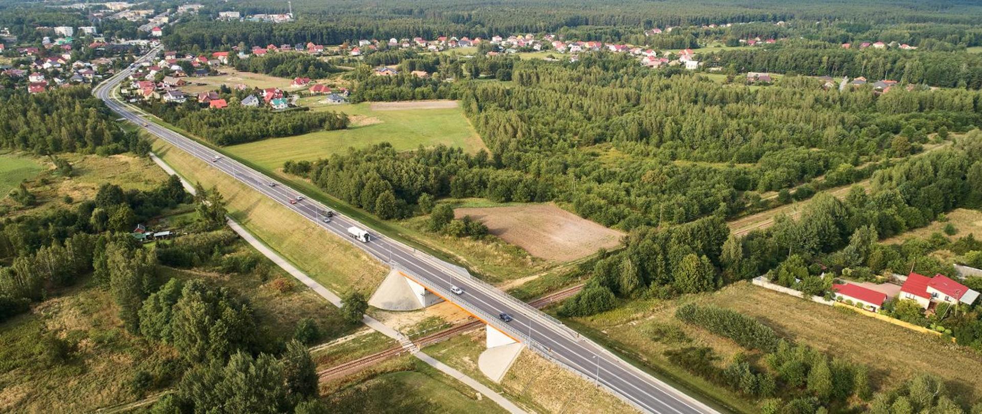 Zdjęcie lotnicze przedstawiające drogę krajową nr 9. Widać jadące samochody, wiadukt nad koleją oraz miasto w oddali. Drzewa są zielone. 