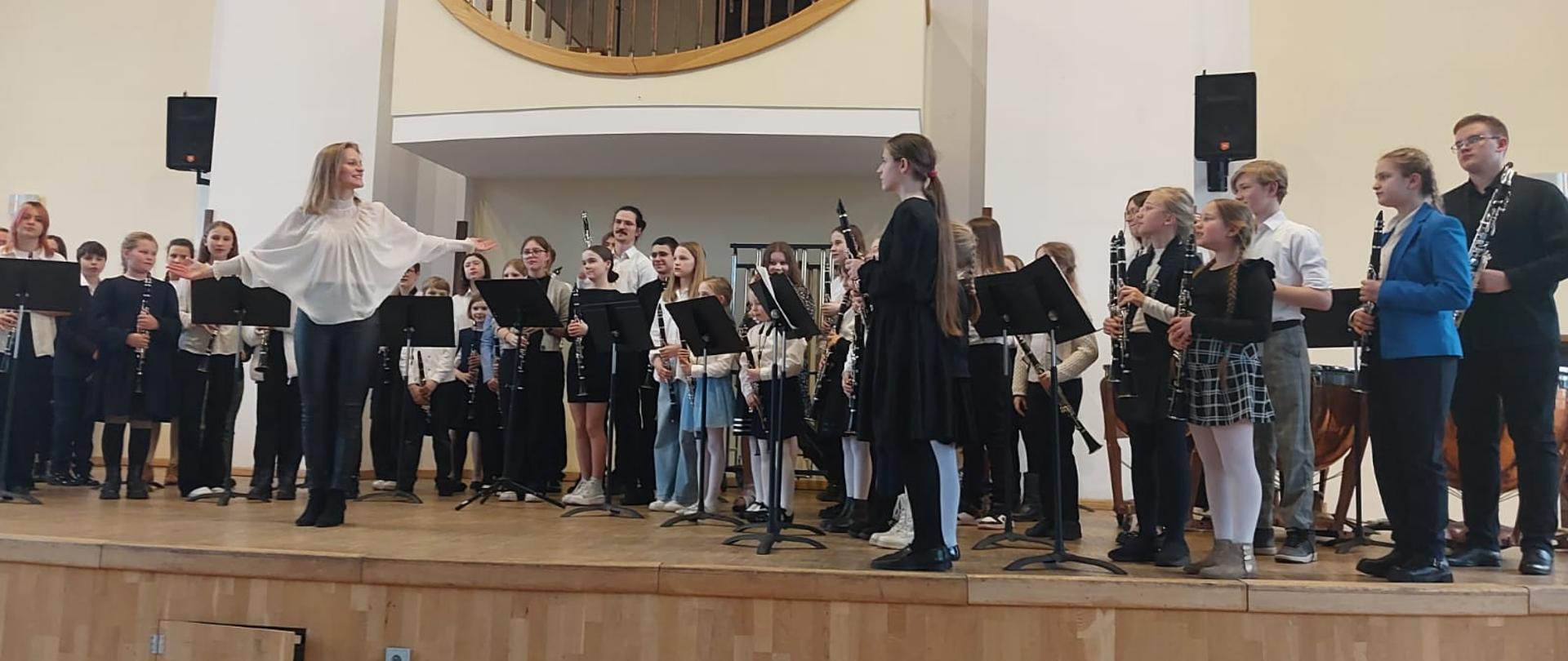 Na scenie w Akademii Muzycznej stoją wykonawcy koncertu klarnetowo - saksofonowego gotowi do ukłonu. Pozuje kilkadziesiąt dzieci i nauczycieli.