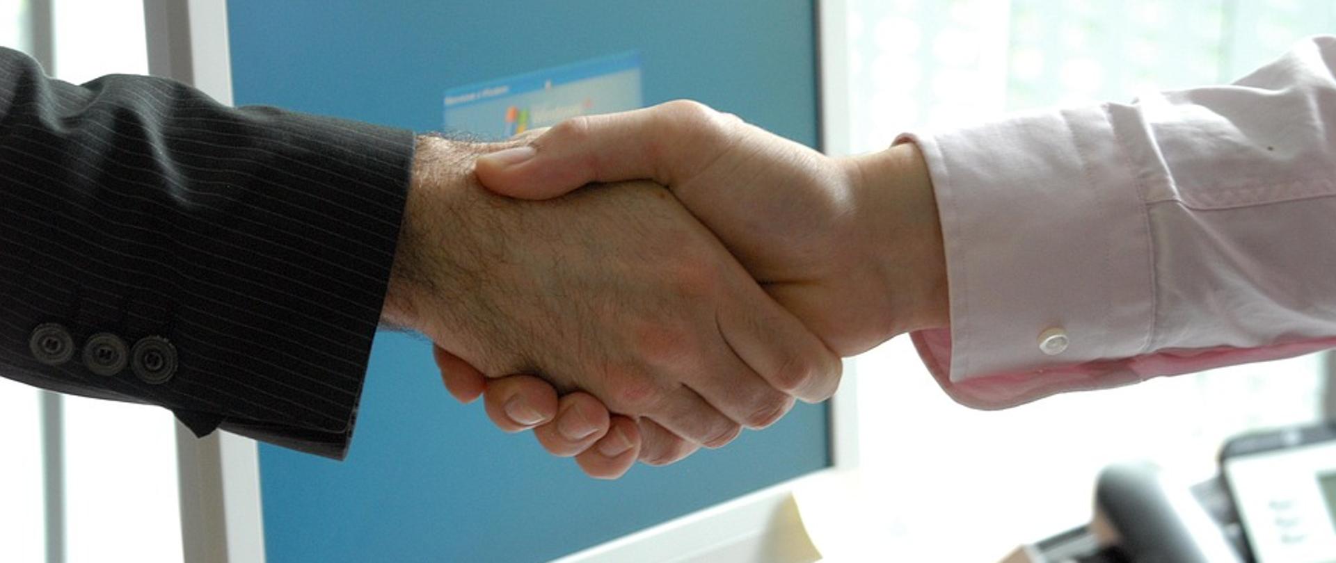 uścisk dłoni, w tle komputer i telefon na biurku