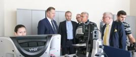 Minister stoi obok grupy ludzi, przed nimi skomplikowana maszyna - drukarka 3D.