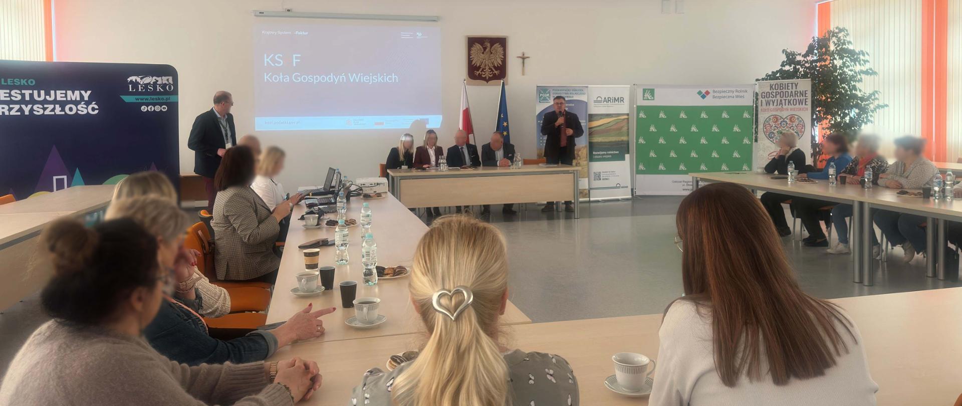 Uczestnicy szkolenia siedzą w sali. Przed nimi są eksperci. Na ekranie wyświetlana jest prezentacja.