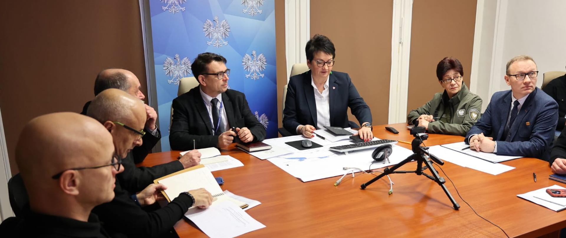Wojewoda Monika Jurek razem z uczestnikami konferencji online zorganizowanej przez Ministerstwo Klimatu i Środowiska. Na zdjęciu oprócz Wojewody widać między innymi Dyrektora Wydziału Bezpieczeństwa i Zarządzania Kryzysowego, Pana Piotra Tarapatę (z lewej strony od Wojewody). Wszyscy siedzą przy stole. 