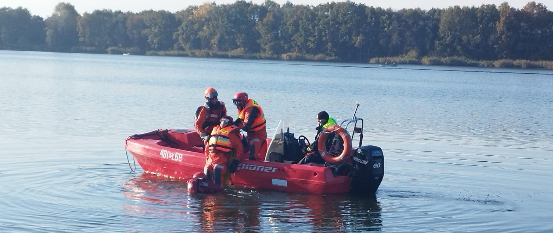 SZKOLENIE Z RATOWNICTWA NA OBSZARACH WODNYCH REALIZOWANEGO PRZEZ KSRG W ZAKRESIE PODSTAWOWYM. Na zdjęciu strażacy podczas szkolenia na jeziorze, strażacy na łodzi i w wodzie ćwiczą ratowanie osoby poszkodowanej.