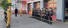 Strażacy stoją na zbiórce przed budynkiem komendy
