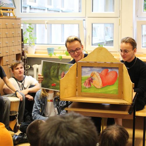 zdjęcie przedstawia uczniów prezentujących opowiadanie na rozkładanym ekranie na stoliku w sali edukacyjnej, inne ujęcie